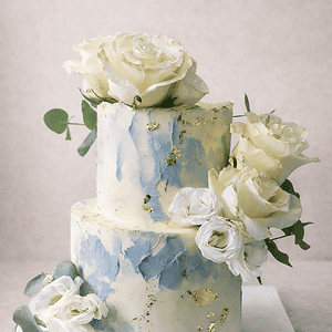 Tarta personalizada de dos pisos con diseño acuarela azul, flores blancas y detalles dorados en Madrid